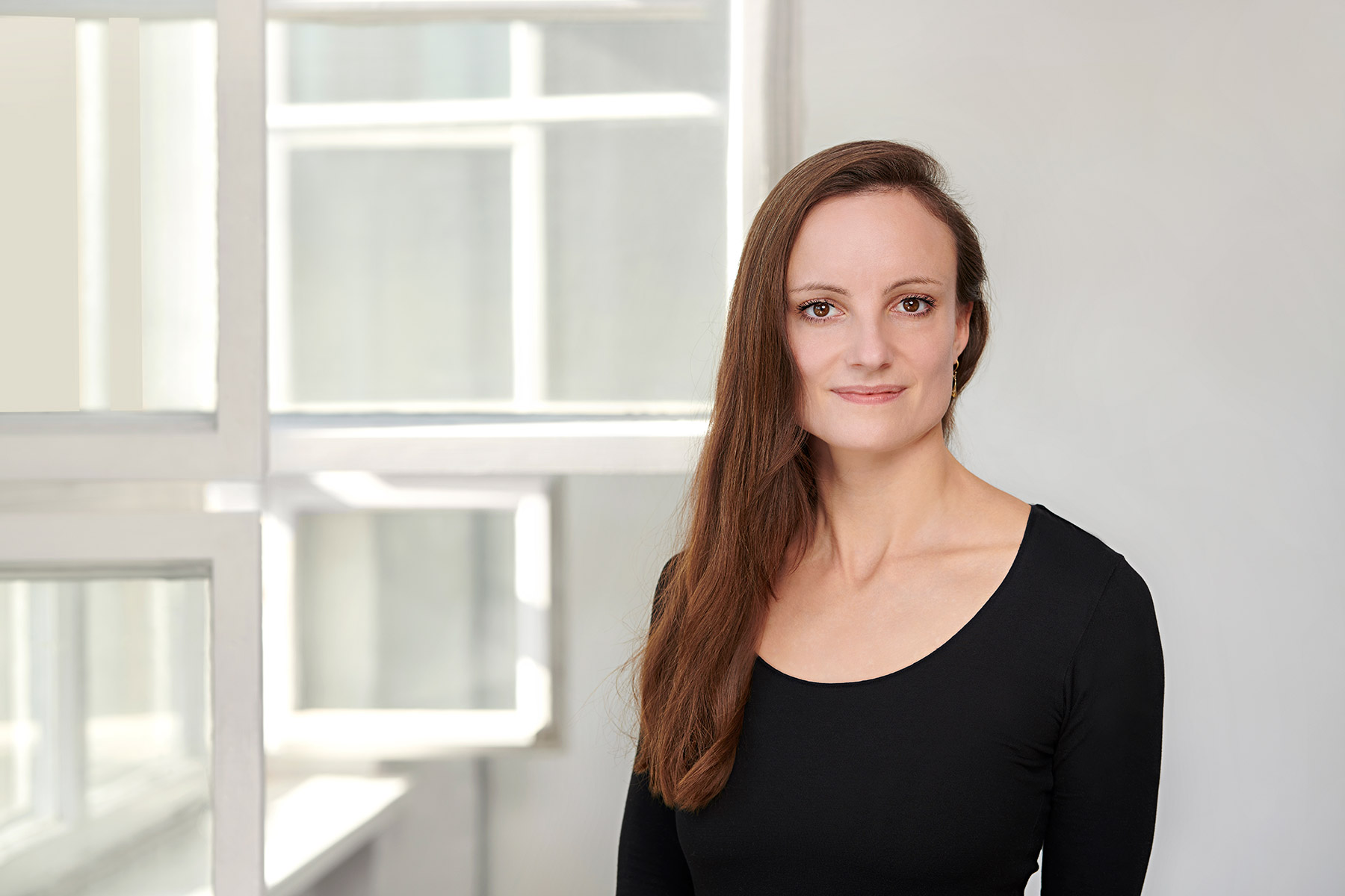 Portraitbild von Anna Stachow vor weißem Hintergrund und seitlich geöffneten Altbaufenstern