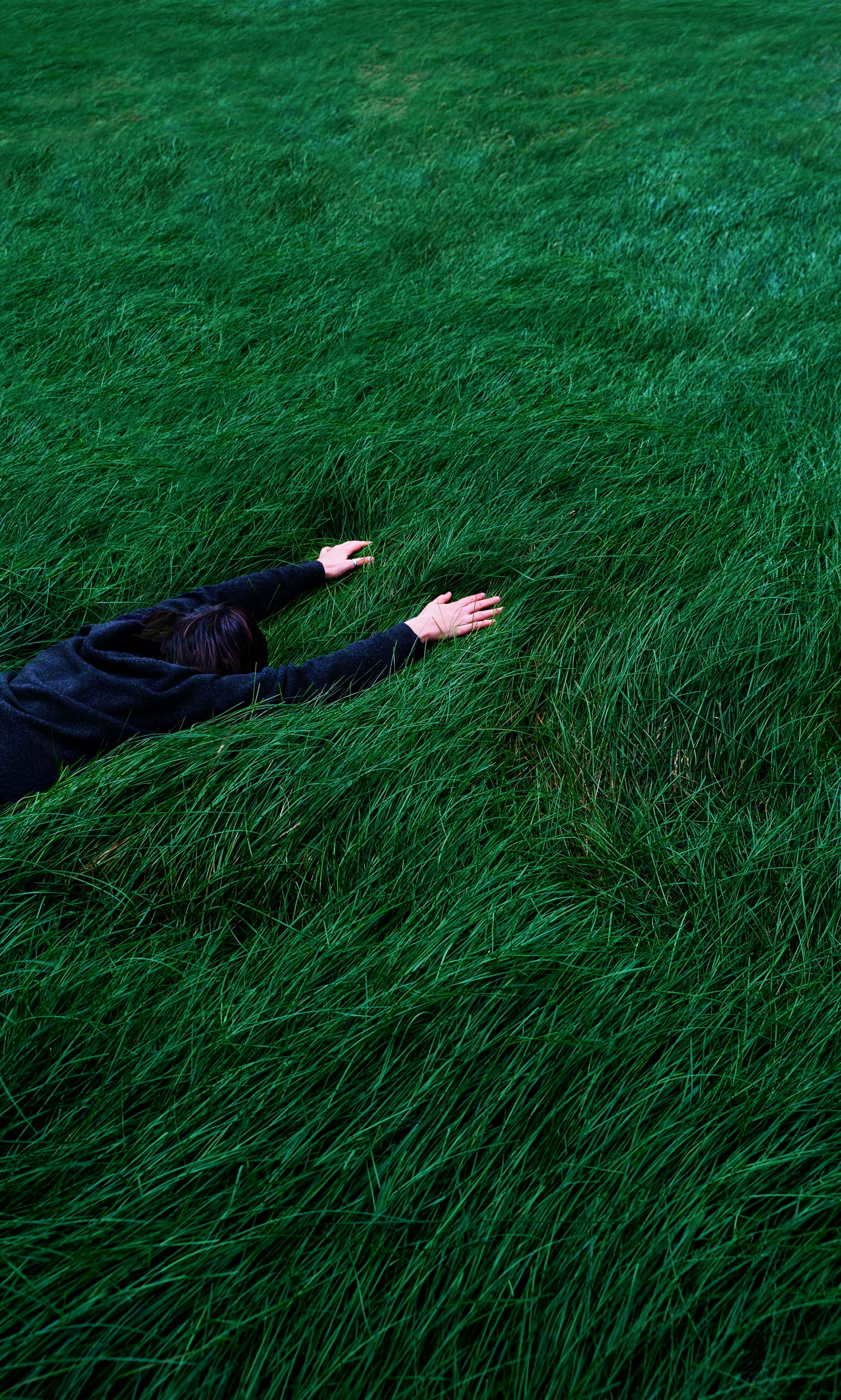 Überforderung – Person liegt bäuchlings in hohem grünen Gras