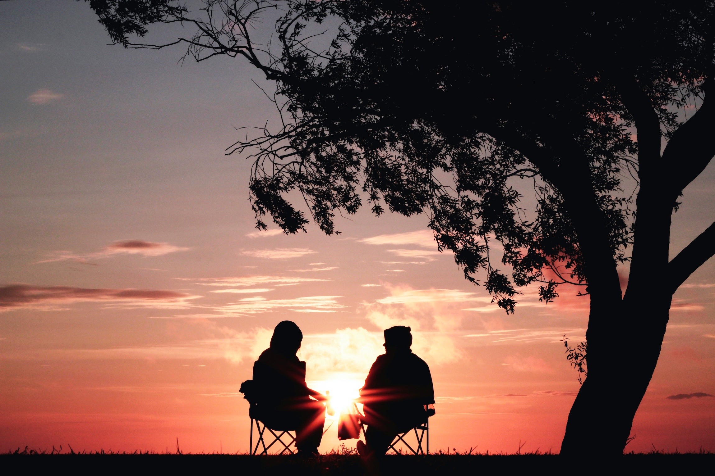 Trigger – Zwei Personen, neben einem Baum auf Stühlen sitzend, vor Sonnenuntergang