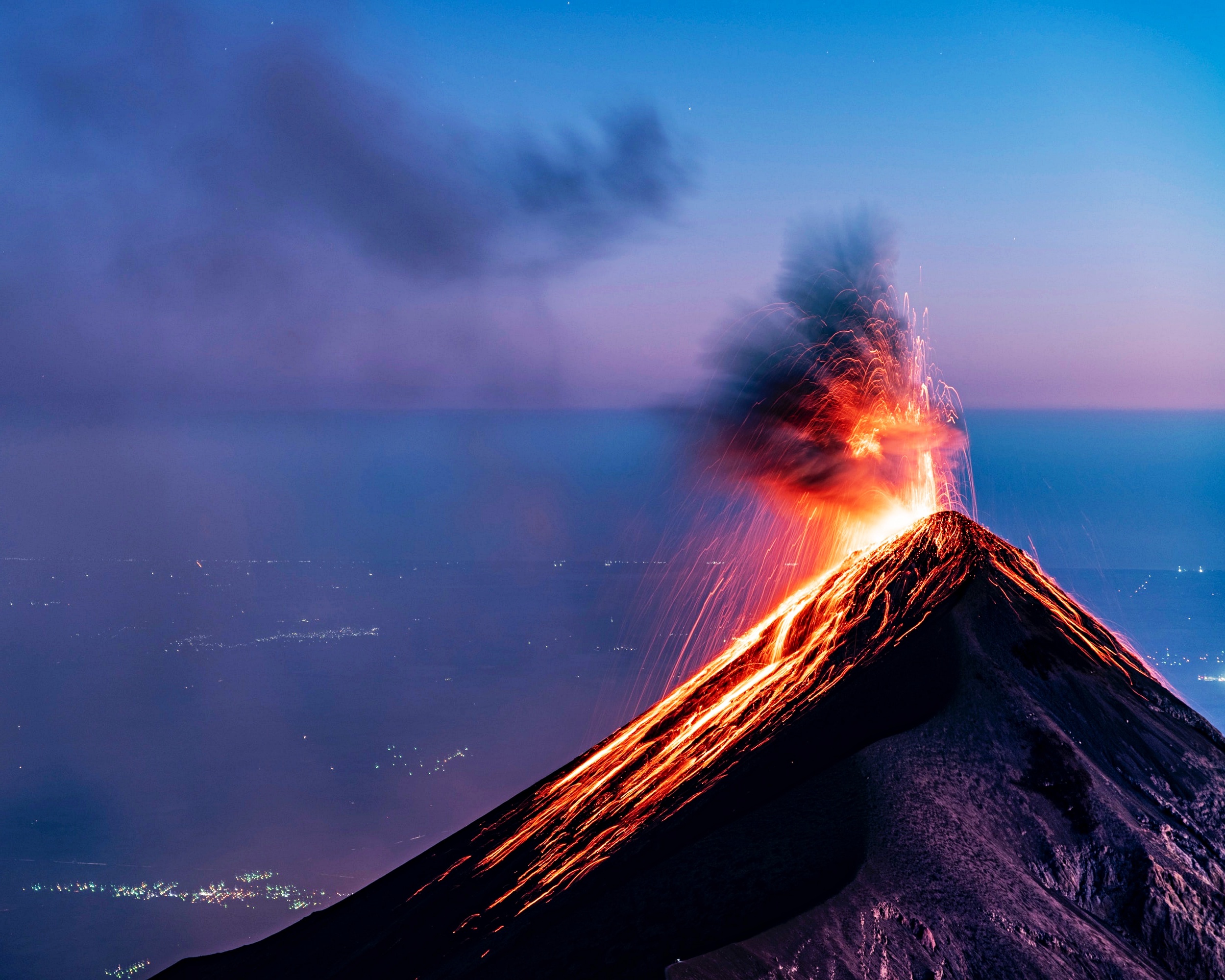 Trigger – Vulkan, der Lava und Rauch spuckt vor blau-lila Horizont