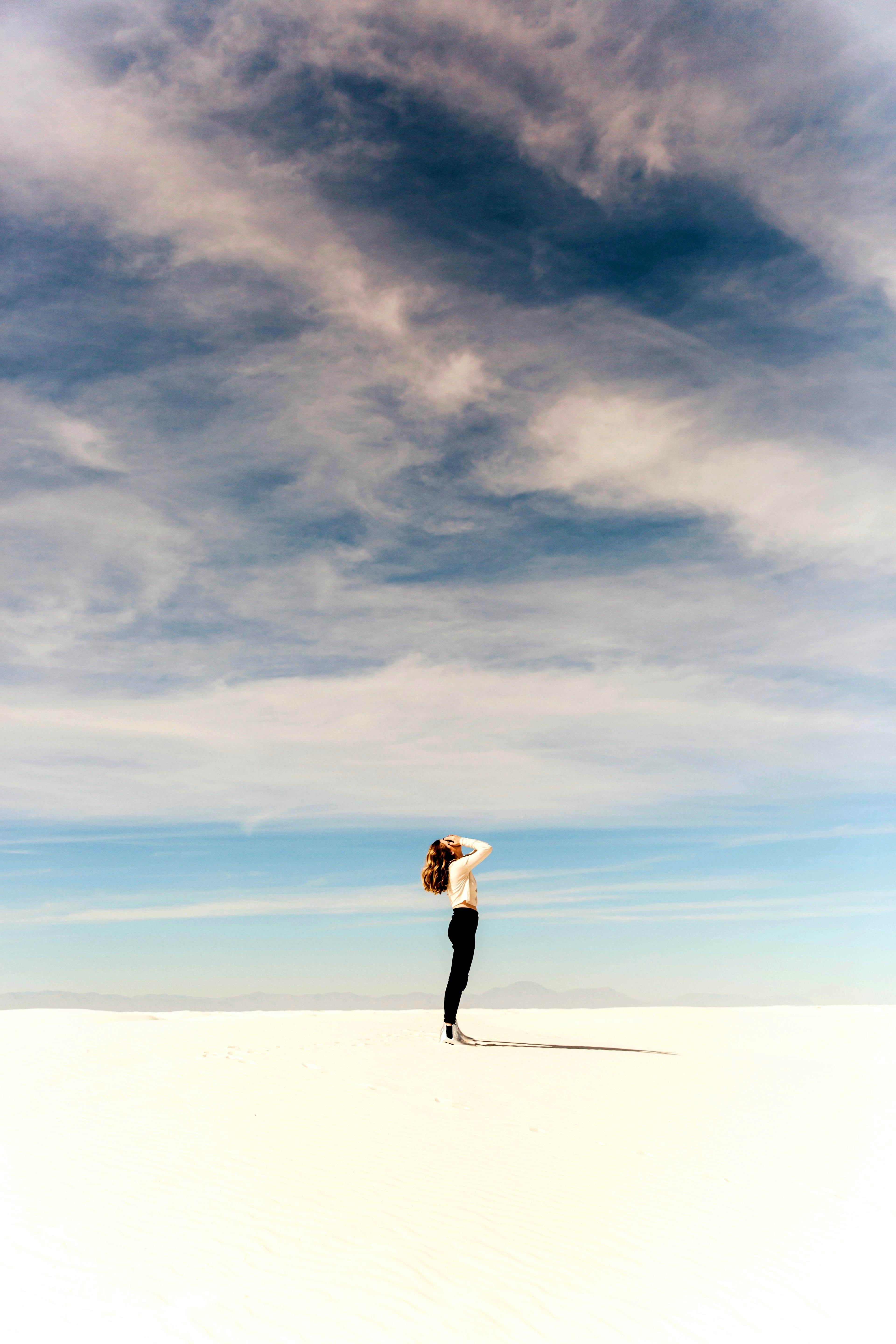 Körper und Geist – Seitlich stehende Frau auf weißem Untergrund vor Horizont mit blauem Himmel und Wolken