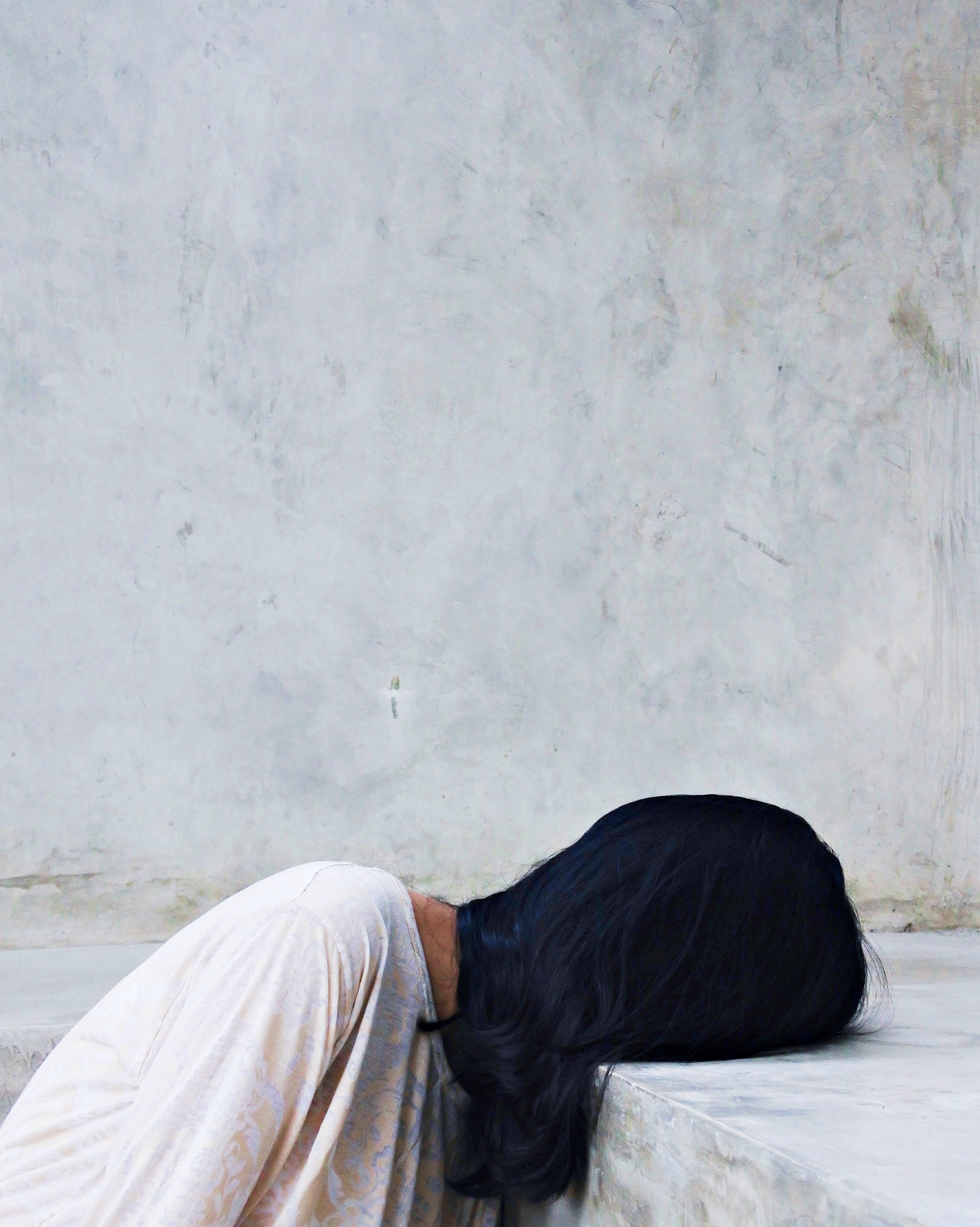 Schuldgefühle – Frau sitzt gebeugt und legt ihren Kopf auf einer Steinkante ab
