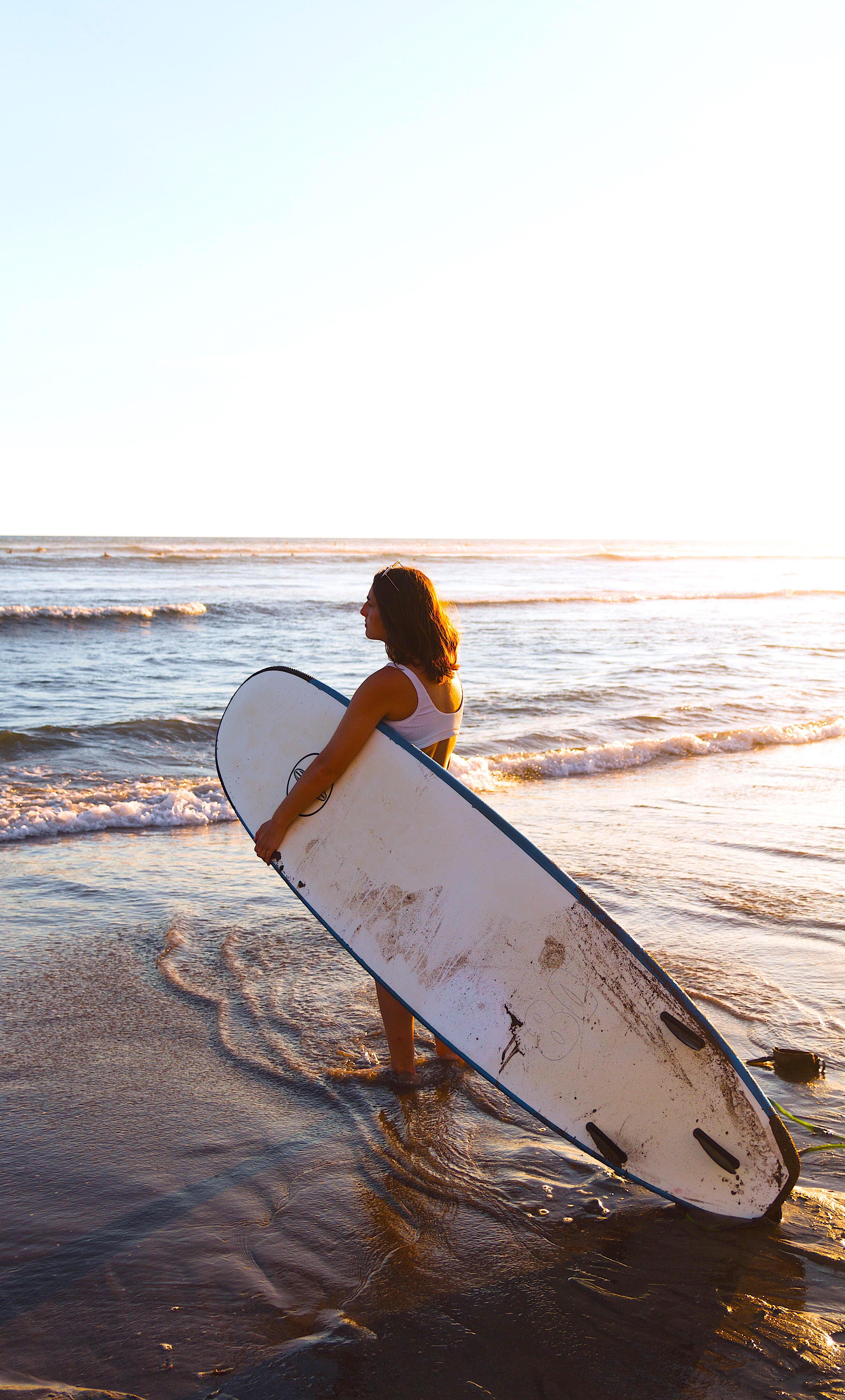 Frau steht am Meeresufer mit Surfboard im Arm