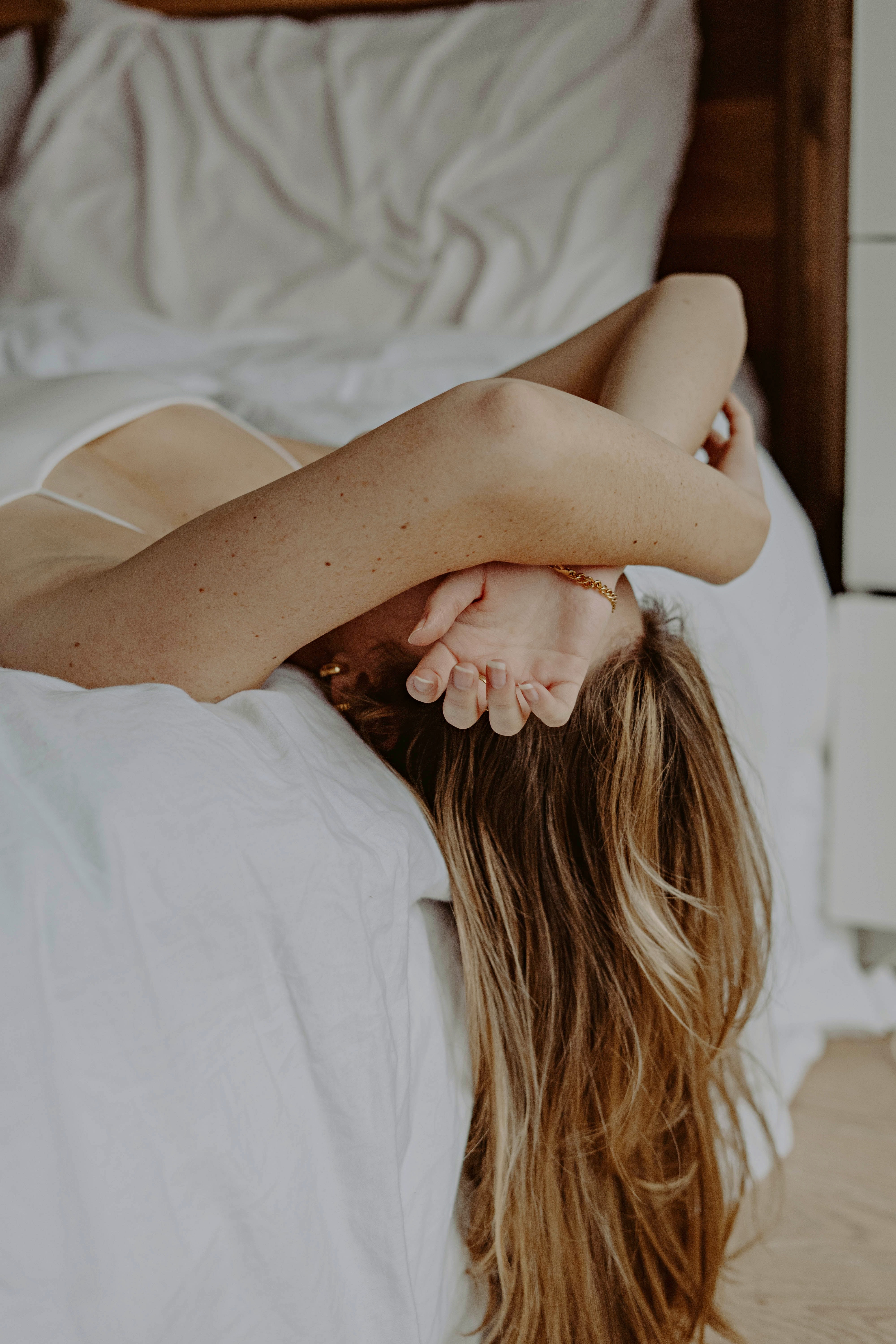 Biorhythmus – Frau liegt quer im Bett und legt ihre Arme über das Gesicht