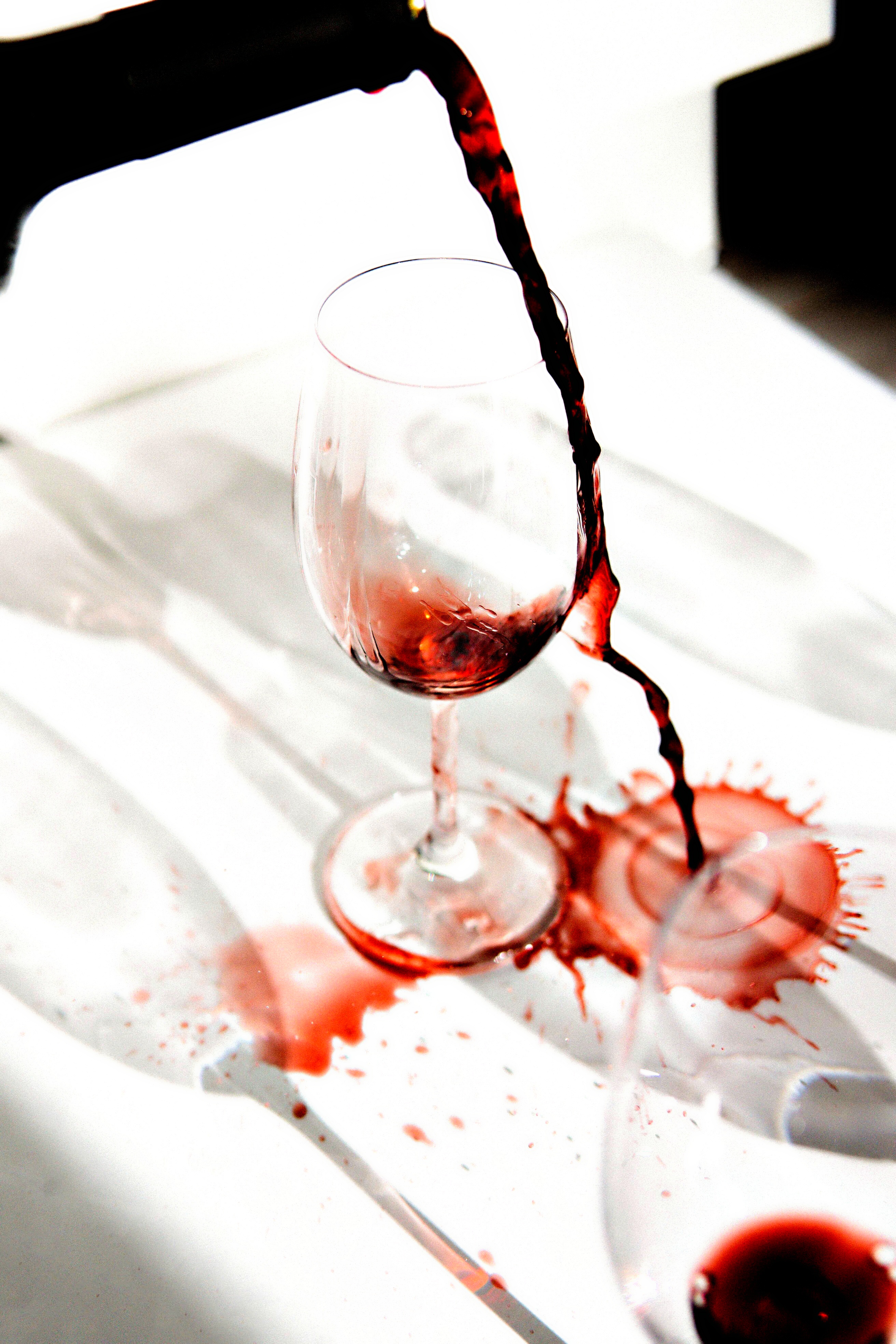 Rotwein wird neben ein Glas auf eine weiße Tischedecke geschüttet