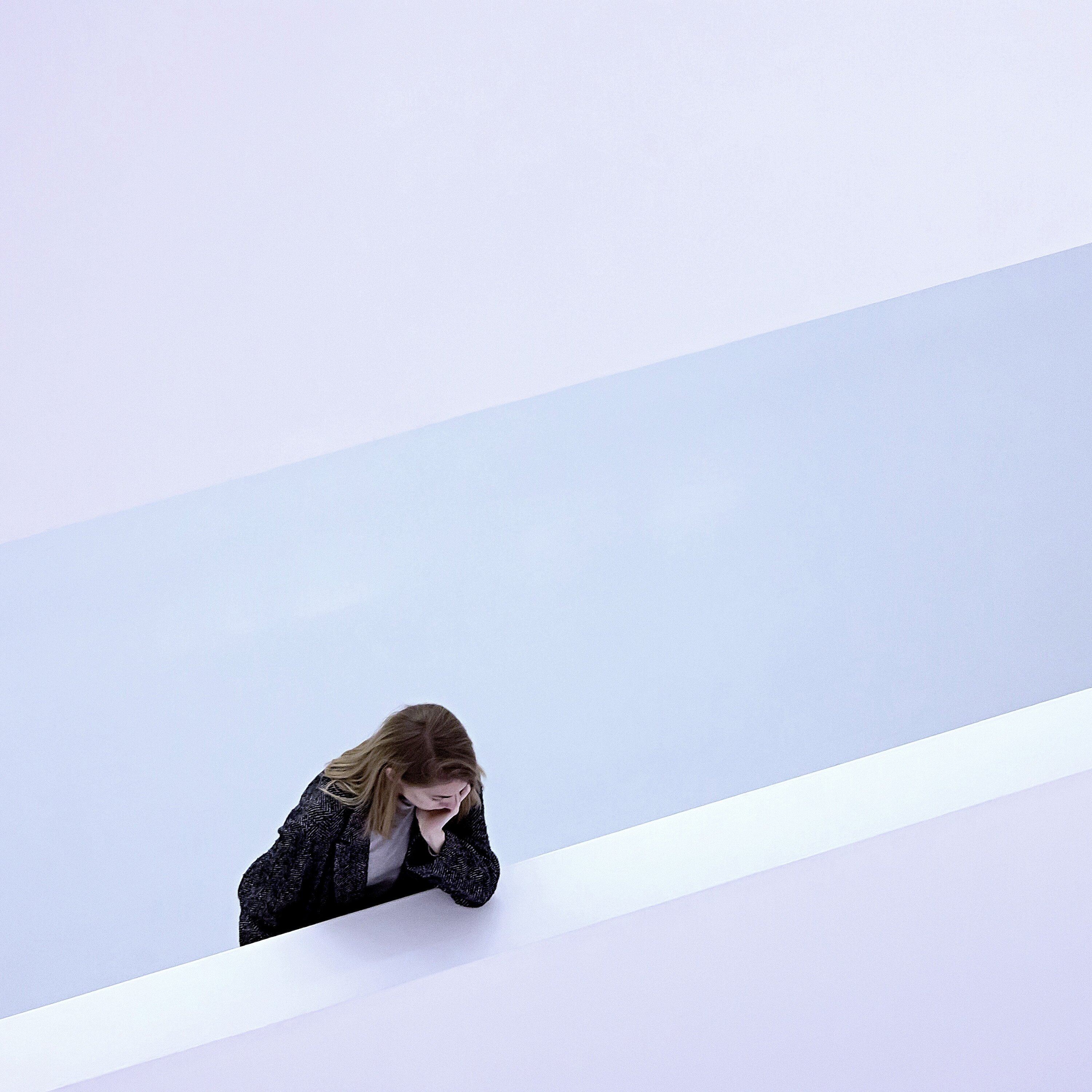 Langhaarige Person steht in hellem Treppenhaus und blickt nachdenklich nach unten